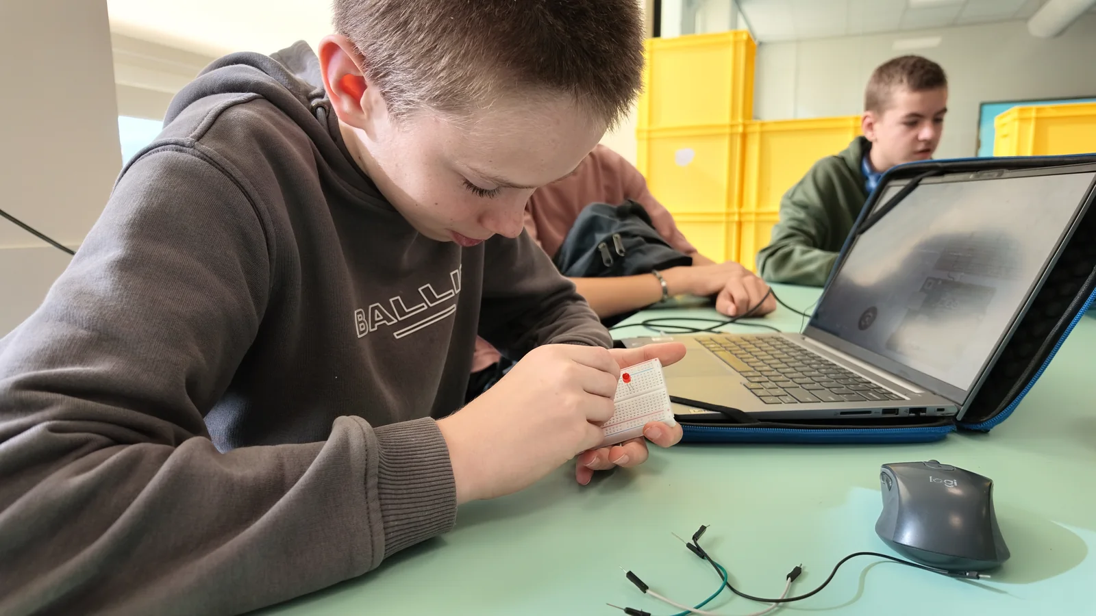 Leerling werkt aan elektronica met een laptop naast de werkplek